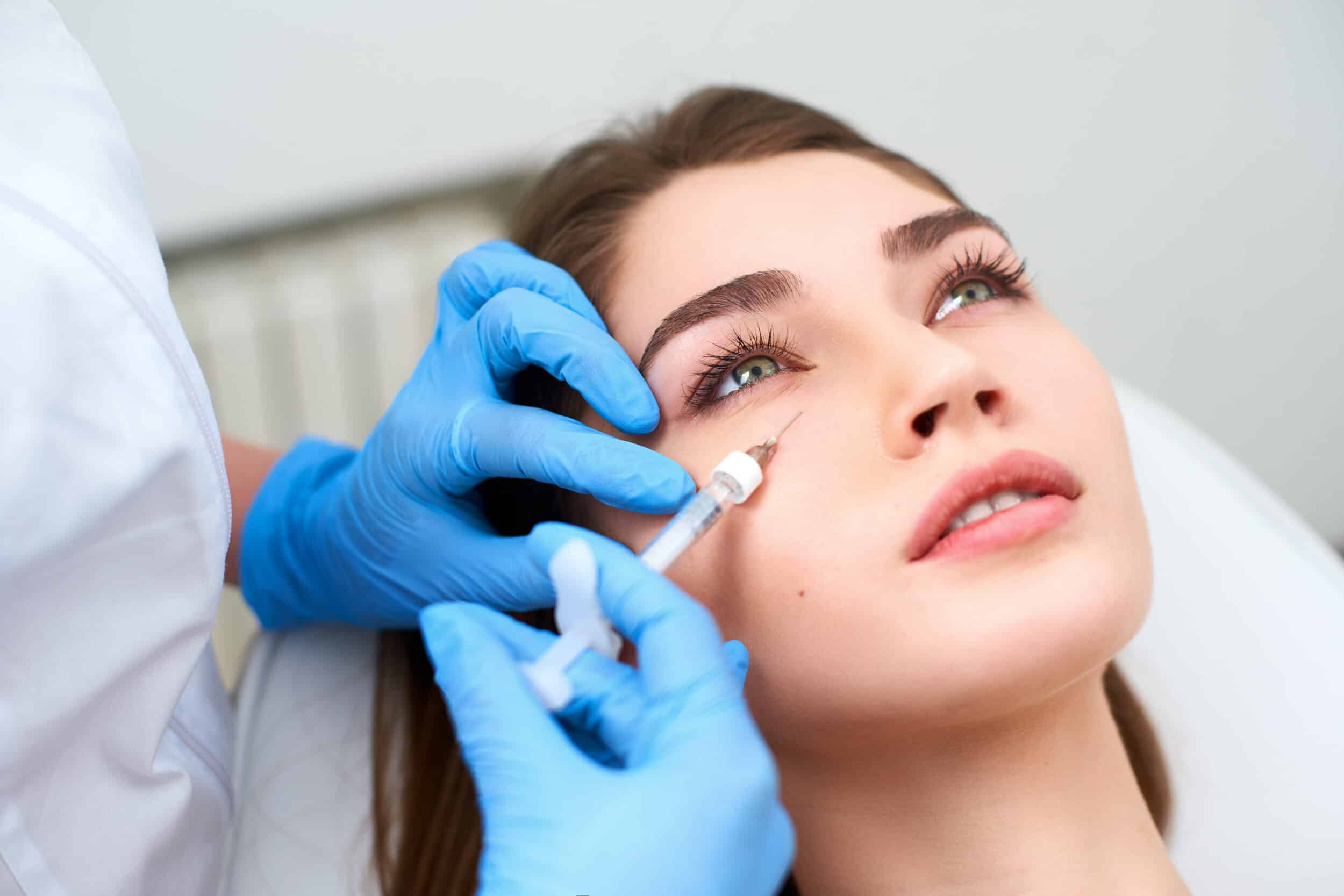Doctor in medical gloves with syringe injects botulinum under eyes for rejuvenating wrinkle treatment. Filler injection for eye wrinkles smoothing. Plastic aesthetic facial surgery in beauty clinic EZ Gel in Henderson